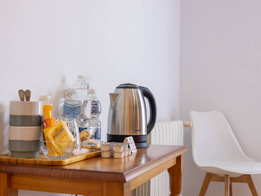 Una mesa de madera con una tetera, botellas de agua, un recipiente de vidrio y una silla.