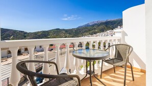 A balcony with a table and chairs, overlooking a mountainous landscape.
