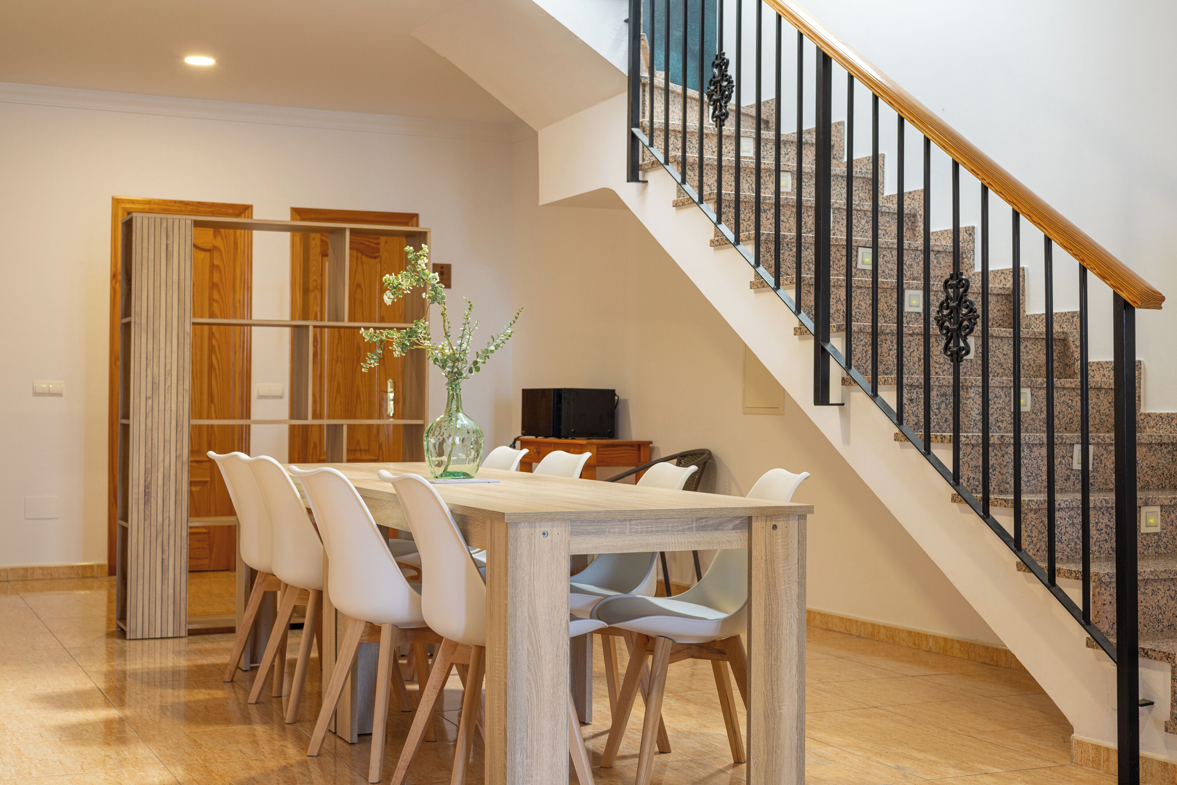 Un comedor con una mesa y sillas, una escalera con barandillas negras y una puerta de madera.