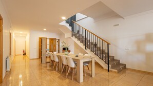 A spacious dining area with a wooden table and chairs, a staircase with a black railing, and a fire extinguisher in the hallway.