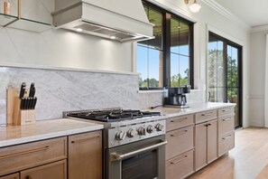 A modern kitchen with a gas stove, oven, and a coffee maker on the counter. - Luxury Country Retreat | Sleeps 15 | Bourbon Trail (Simpsonville)