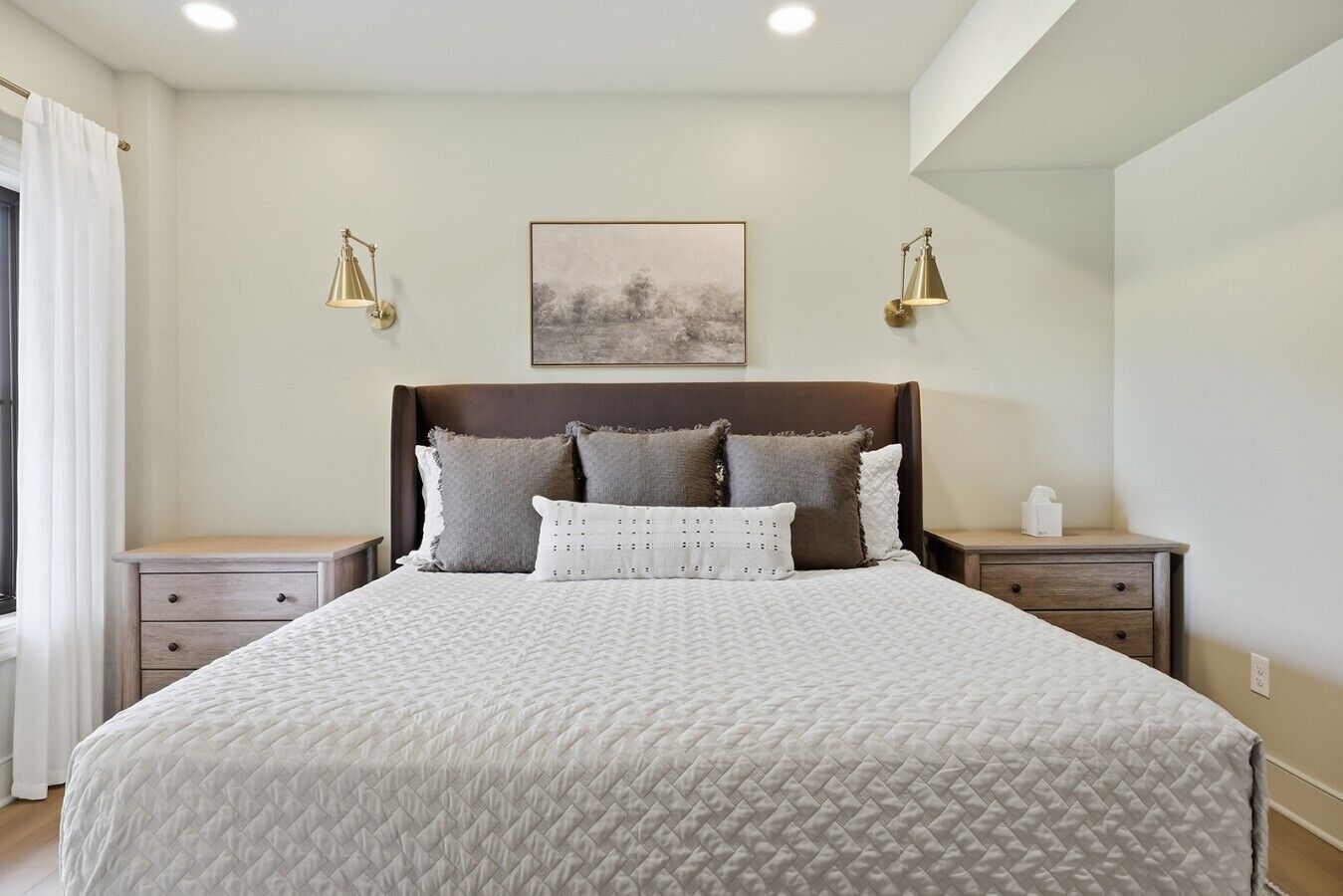 A neatly made bed with a quilted cover, two bedside tables with lamps, and a framed picture on the wall.