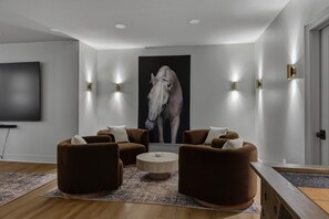 A modern living room with a large flat-screen TV, two brown sofas, a coffee table, and a wall-mounted horse painting. - Luxury Country Retreat | Sleeps 15 | Bourbon Trail (Simpsonville)