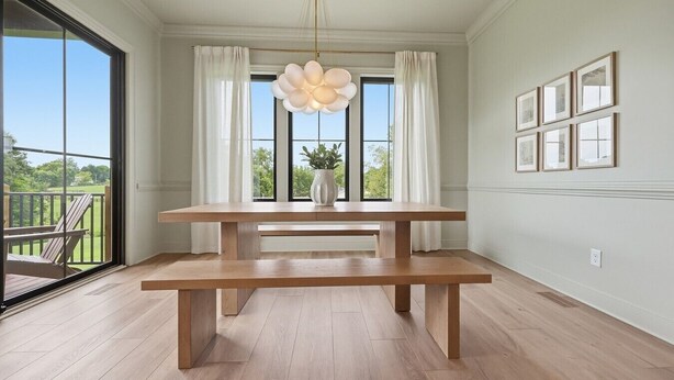 Ein Essbereich mit Holztisch und Bänken, großen Fenstern mit Vorhängen und Blick ins Freie.