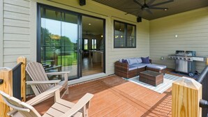 Eine überdachte Terrasse mit Gartenmöbeln, einem Grill und einer Schiebetür zu einem Innenbereich.