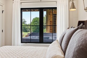 Ein Schlafzimmer mit großem Fenster, einem Bett mit Kissen und Blick auf eine Außenwhirlpool-Badewanne.