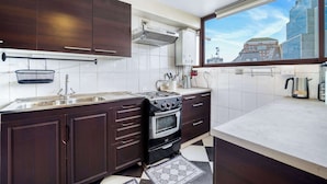 Una cocina moderna con gabinetes de madera oscura, un lavamanos de acero inoxidable, un horno empotrado y una ventana con vistas a la ciudad.