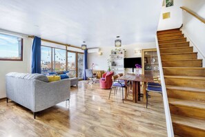 A spacious living area with a sofa, dining table, chairs, and a staircase. - Dúplex Skyline apartment 2D Wifi Near Costanera Center (Providencia)