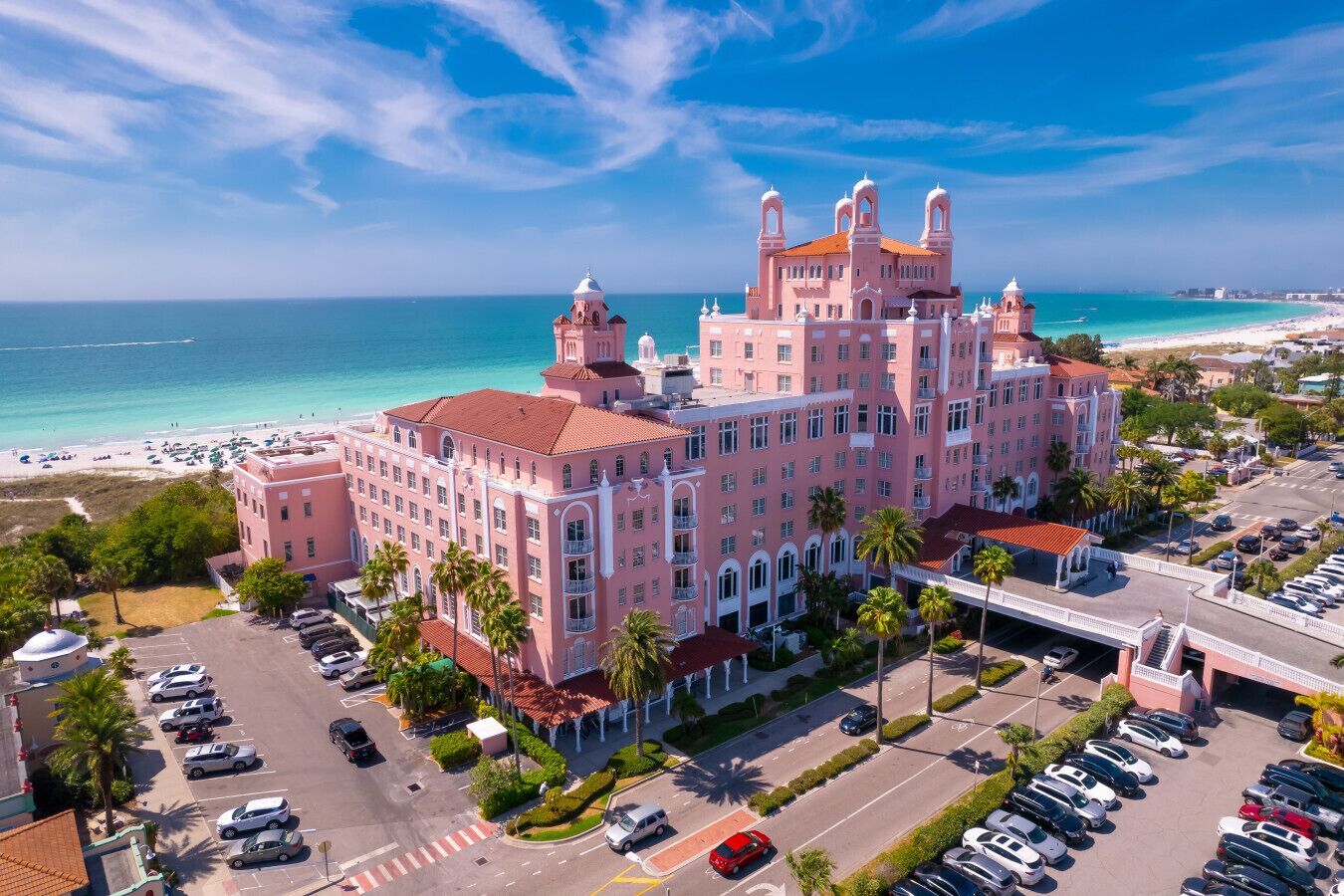 A pink hotel with a beach view, parking lots, and a clear sky.