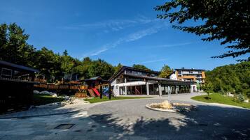 Ein modernes Gebäude mit Glasfassade, einer Holzterrasse und einer begrünten Anlage mit Springbrunnen.