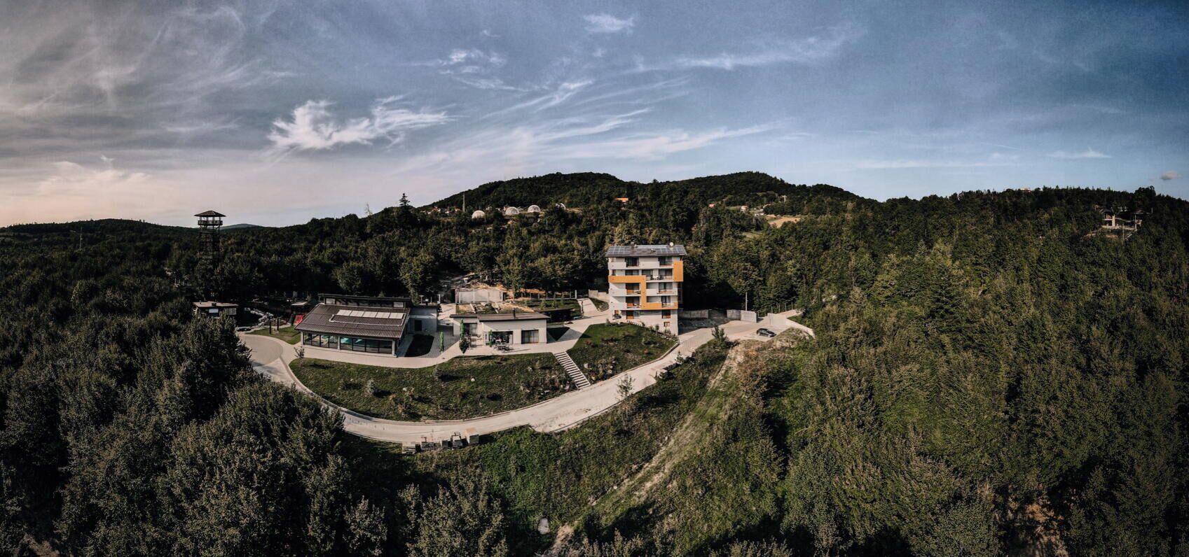 Un conjunto arquitectónico moderno con varias edificaciones, rodeado de un bosque denso y colinas.