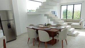 A modern kitchen with a built-in refrigerator, a dining area with a wooden table and white chairs, and a staircase with a unique design.