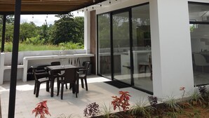 A modern two-story house with a covered patio, outdoor seating, and a large window.