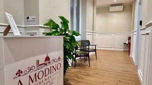 A reception area with a sign for 'A Modino Firenze Suites,' a potted plant, a chair, and a wooden floor. - A Modino Florence Centre Suites (Florence)