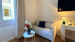 A room with a sofa, a small table with a vase of flowers, a lamp, and a television on the wall. - A Modino Florence Centre Suites (Florence)