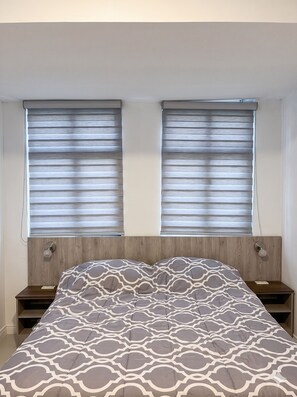 A bedroom with a bed, two bedside tables, and two windows with blinds. - Historic Center Quito by Otium (Quito)