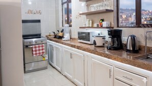 A kitchen with white cabinets, a stove, a microwave, a coffee maker, and a window with a city view. - Historic Center Quito by Otium (Quito)