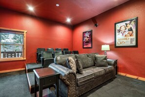 A cozy room with a red wall, a leather sofa, a small table, a poster of The Wizard of Oz, and a window with a view. - Beaver's Mountaintop Retreat! Pool Cabin | Top 5% (Pigeon Forge)