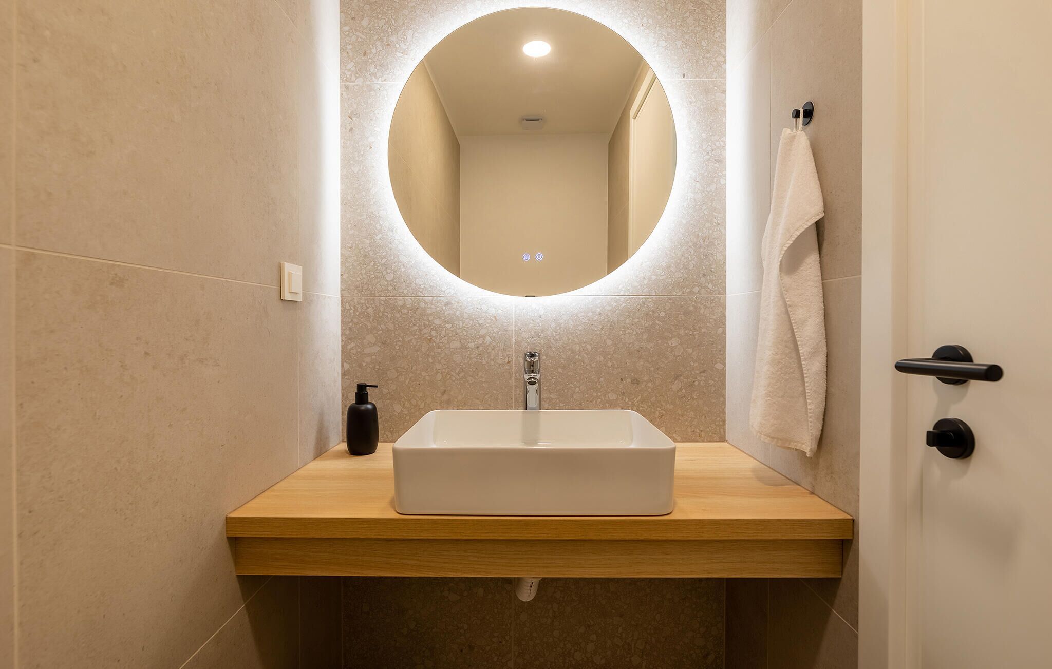 Un bagno con un lavabo rettangolare, uno specchio rotondo e un asciugamano appeso al muro.