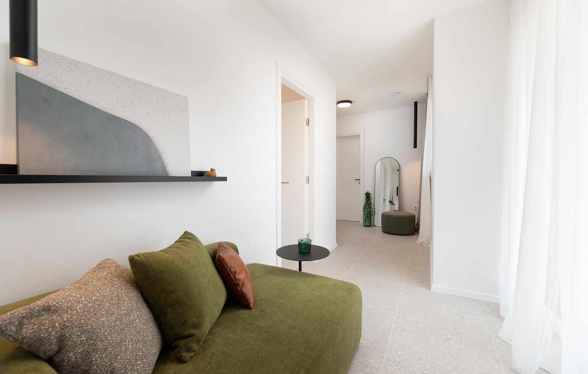 Ein modernes Wohnzimmer mit einem grünen Sofa, einem runden Tisch und einem minimalistischen Kunstwerk an der Wand.