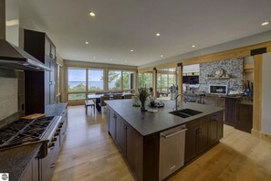 A modern kitchen with a large island, built-in appliances, and a stone fireplace. - Spyglass Ridge Retreat – 6BR Luxury Bay View Pines Estate in Suttons Bay (Suttons Bay)