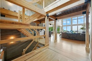 A spacious interior with a wooden staircase, large windows, and a modern living area. - Spyglass Ridge Retreat – 6BR Luxury Bay View Pines Estate in Suttons Bay (Suttons Bay)