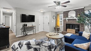 Un salon avec une cheminée, un ventilateur de plafond, un téléviseur et une table basse.