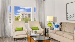 A hotel room with two armchairs, a sofa, a coffee table, a lamp, and a view of a building through large windows. - Marriott Grande Vista  Resort 2 bed/2 Bath w Kitchen in Orlando near Theme Parks (Orlando)