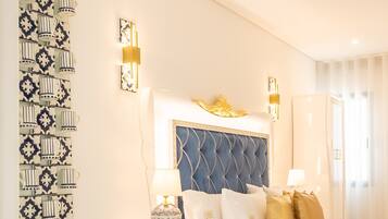 A hotel room with a tufted headboard, decorative wall sconces, a patterned wall art piece, and a bedside table with a lamp.