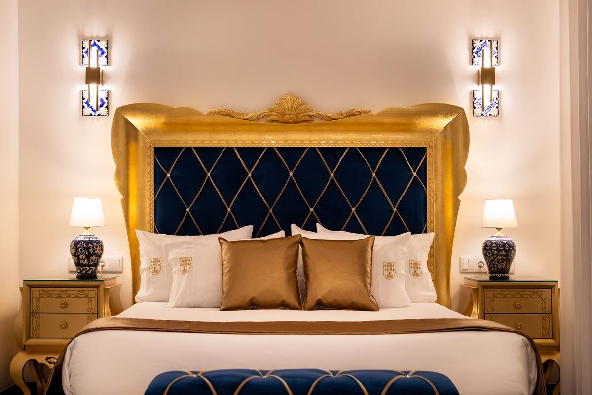 A luxurious bed with a gold headboard, white and brown pillows, and matching nightstands with lamps.