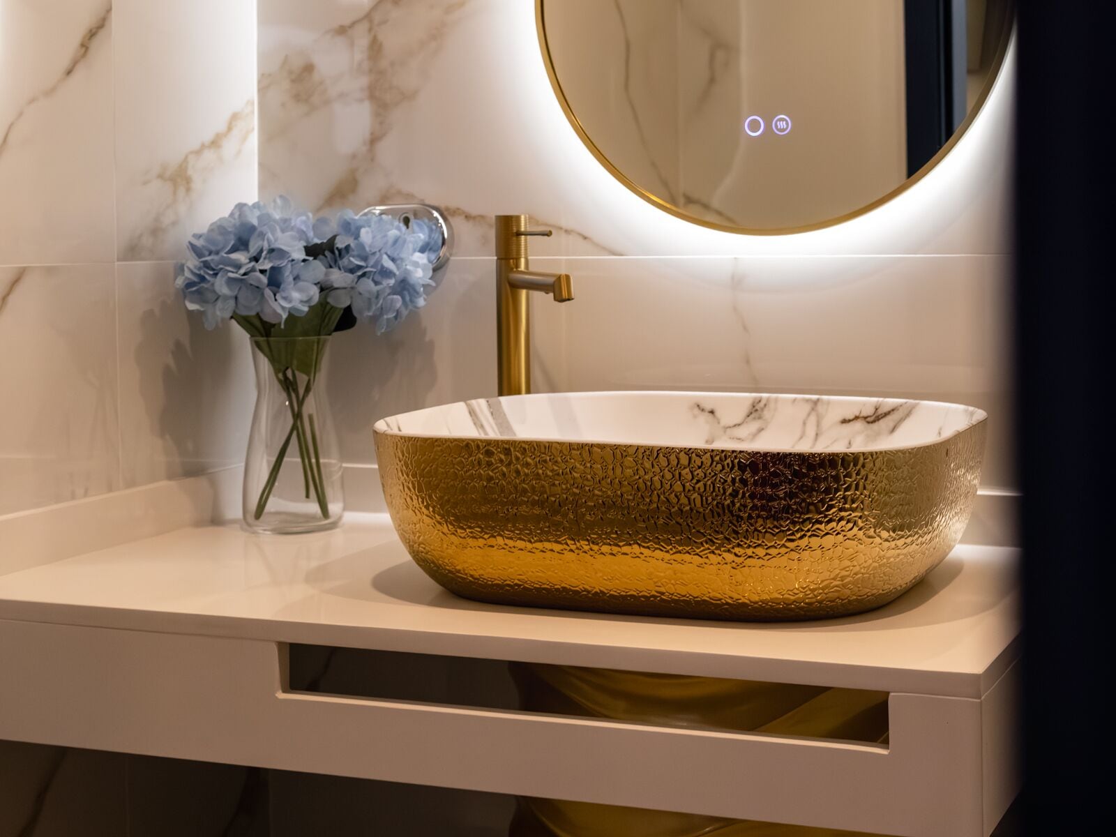 A bathroom with a gold bowl sink, a mirror, and a vase with blue flowers.