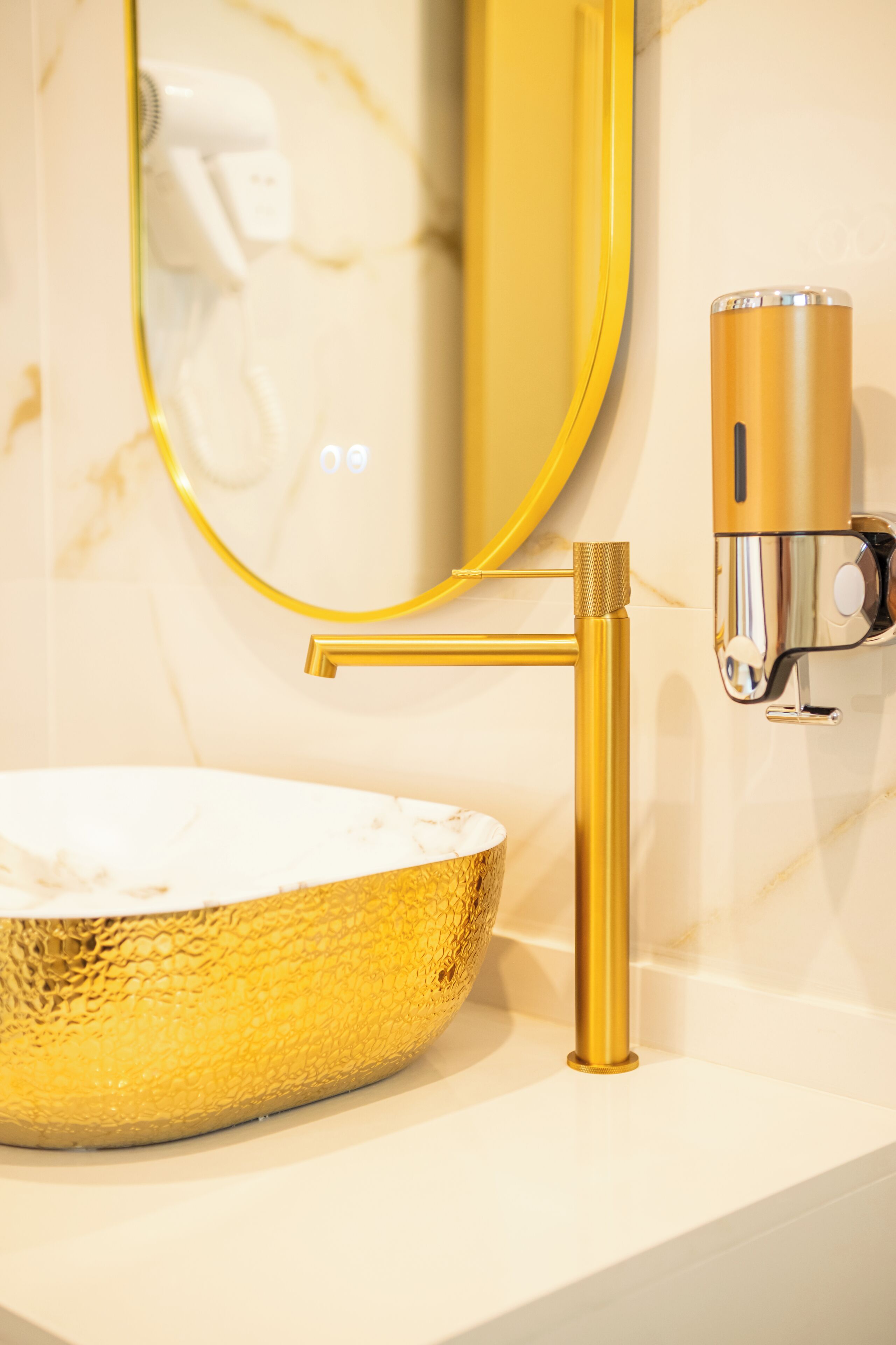 Un baño con lavamanos, grifo y dispensador de toallas dorados.