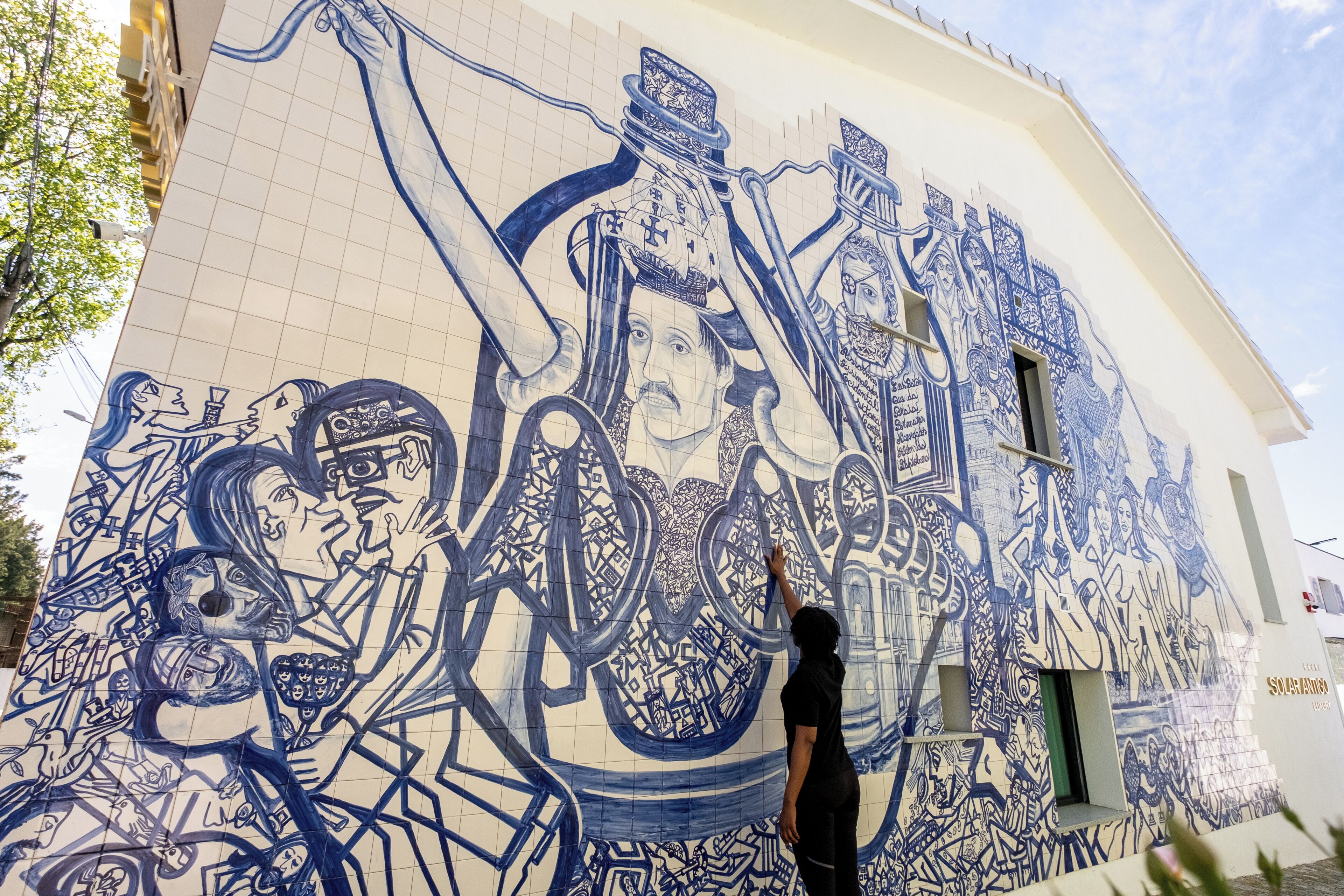Une personne est en train de peindre une grande fresque sur le mur extérieur d’un bâtiment.