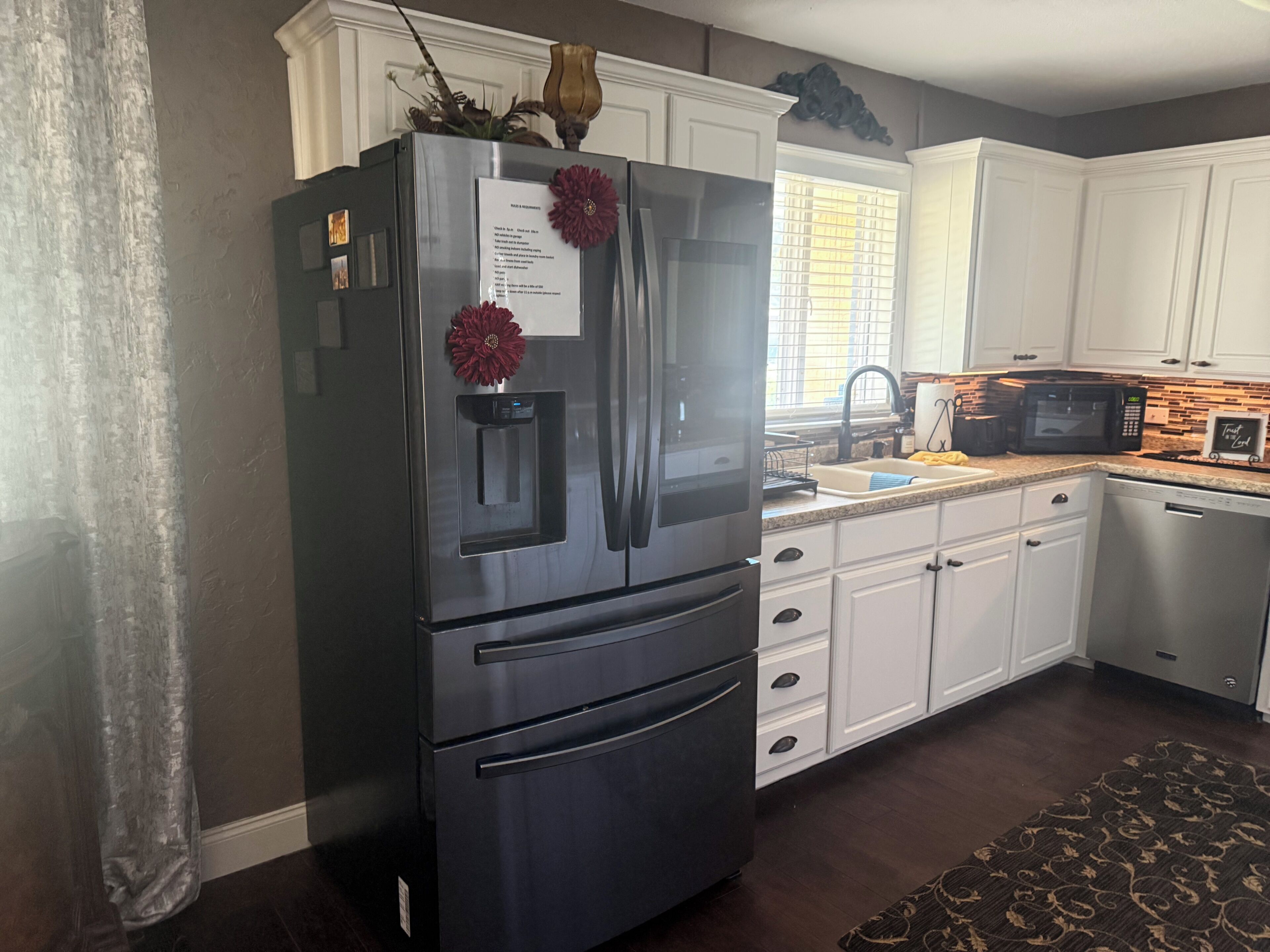 Una cocina con refrigerador de acero inoxidable, armarios blancos, microondas y lavavajillas.