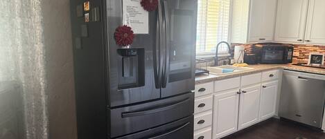 Una cocina con refrigerador de acero inoxidable, armarios blancos, microondas y lavavajillas.
