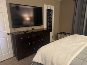 A bedroom with a bed, a dresser, a television on the wall, and a door with a decorative panel. - Delightful 4-bedroom house with AC in lively Lubbock (Lubbock)