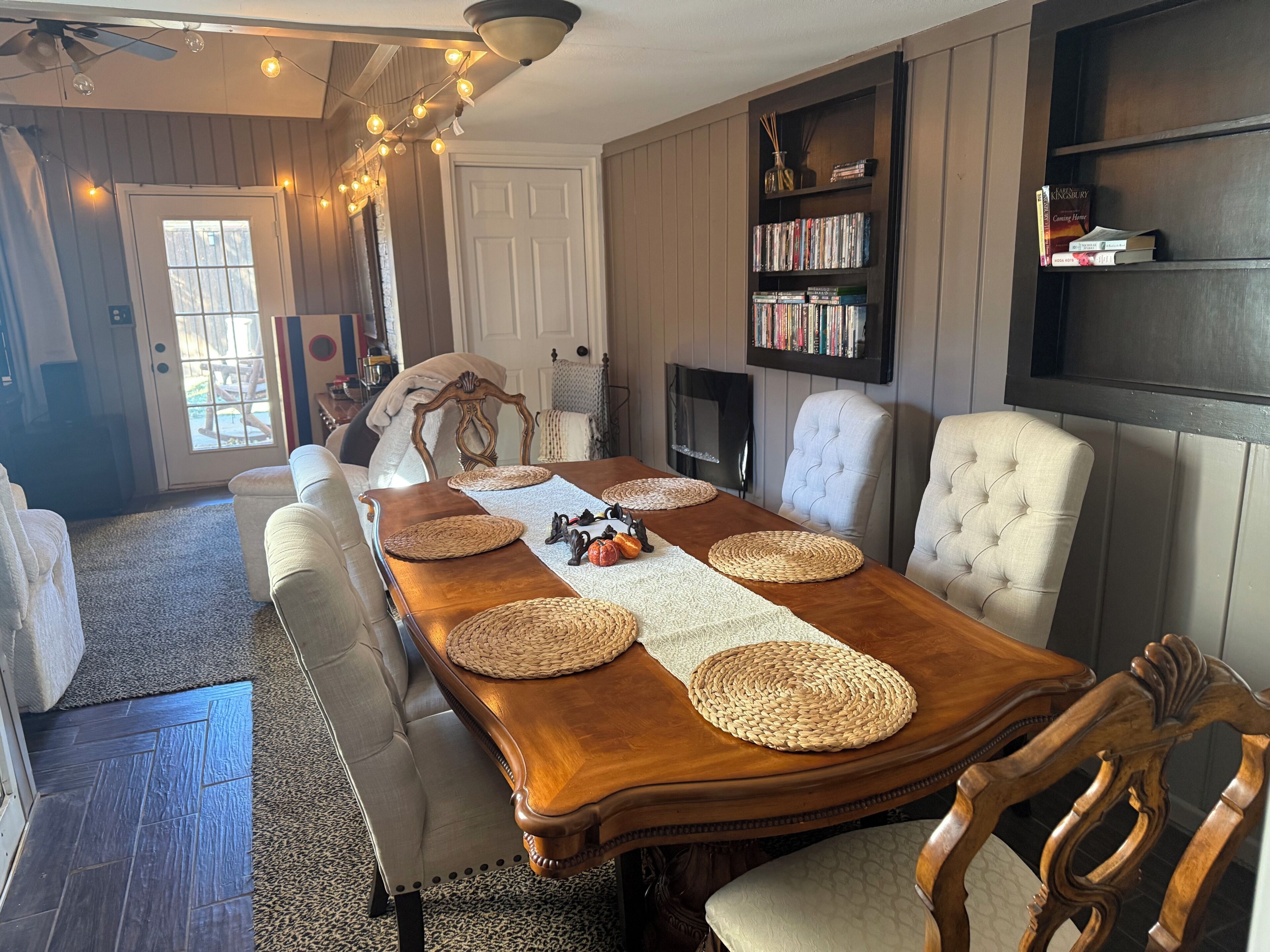 Comedor con una mesa de madera, individuales tejidos y una estantería con libros.
