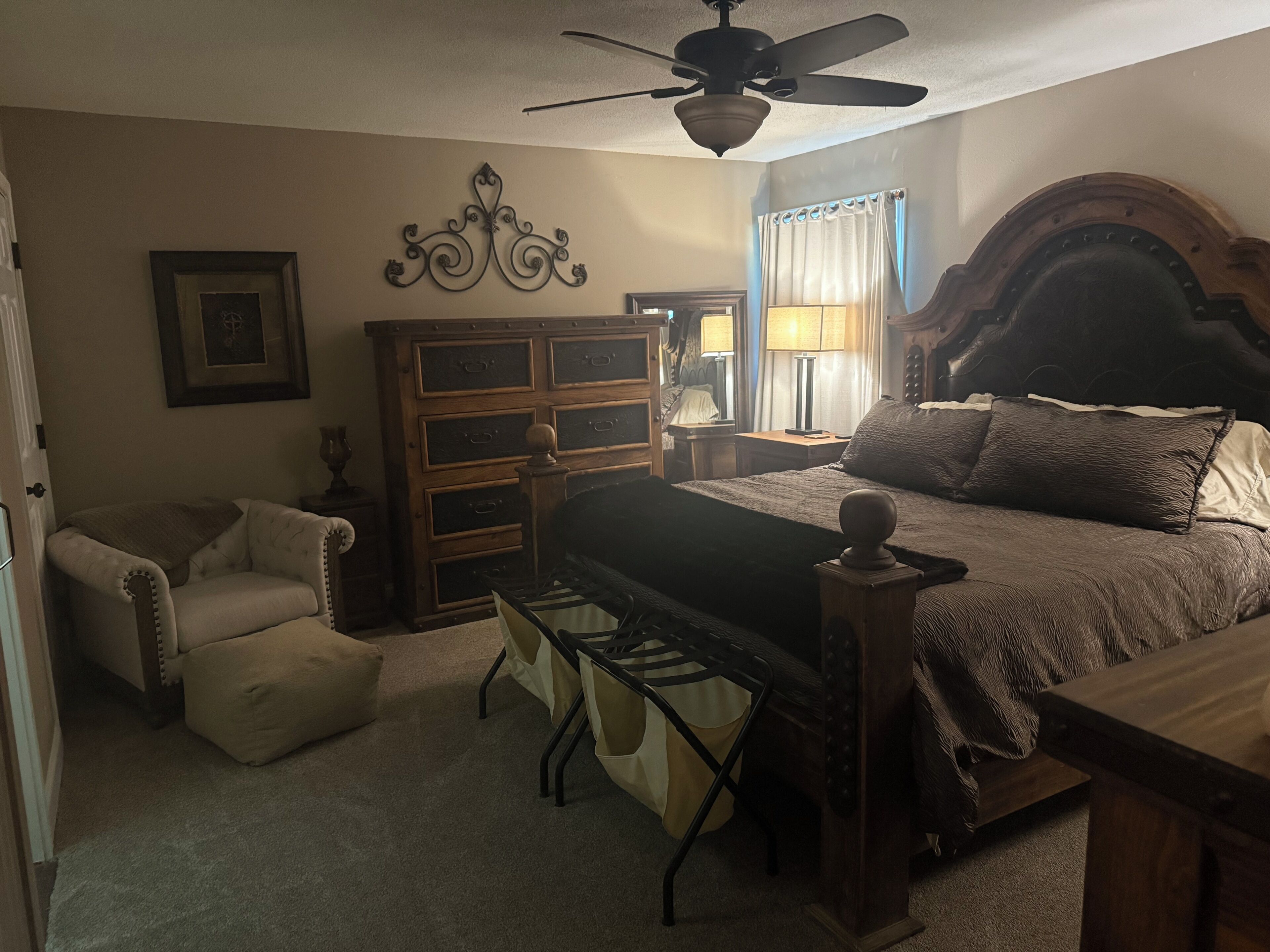 A bedroom with a bed, a chair, a desk, a dresser, and a ceiling fan.