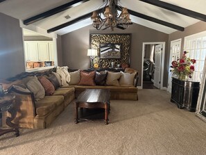 A living room with a sectional sofa, a wooden coffee table, a chandelier, and a decorative wall piece. - Delightful 4-bedroom house with AC in lively Lubbock (Lubbock)