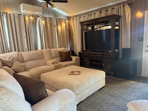 A living room with a sectional sofa, a flat-screen TV, and a dark wooden entertainment center. - Delightful 4-bedroom house with AC in lively Lubbock (Lubbock)