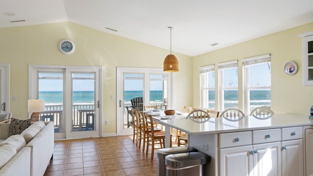 A kitchen with a view of the ocean, a dining area with chairs, and a white cabinet with drawers. - aOceanfront | Incredible Views | Steps to the Beach (Surf City)