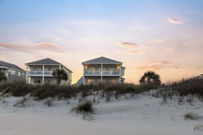 Ein Strandgrundstück mit mehreren Gebäuden, darunter ein zweistöckiges Haus mit Balkon und ein größeres Haus mit Dachterrasse.