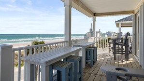 A wooden deck with white railings, a bench, and a table with chairs, overlooking a beach. - aOceanfront | Incredible Views | Steps to the Beach (Surf City)