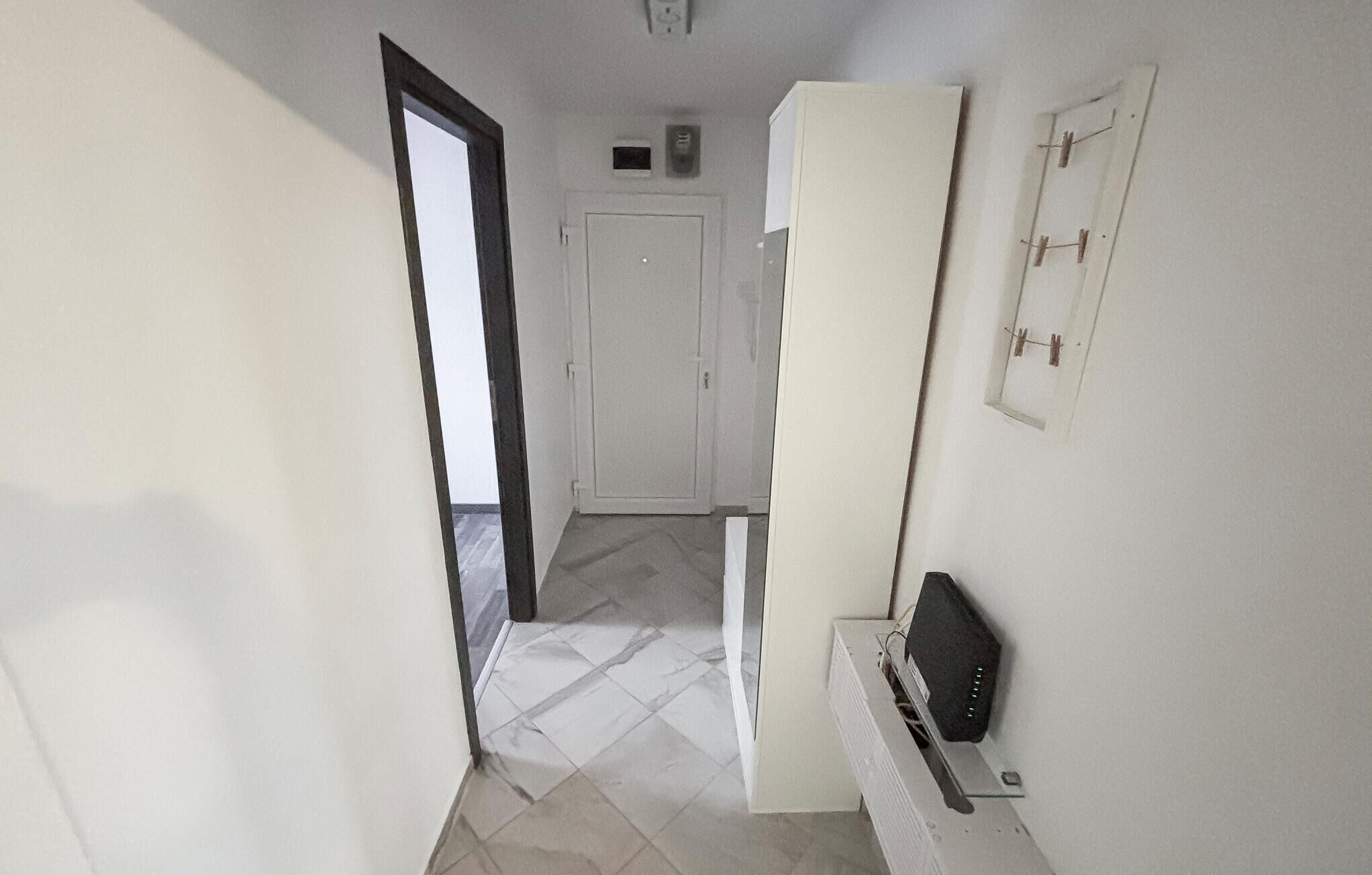 A hallway with a white door, a white wardrobe, and a small black device on a white surface.