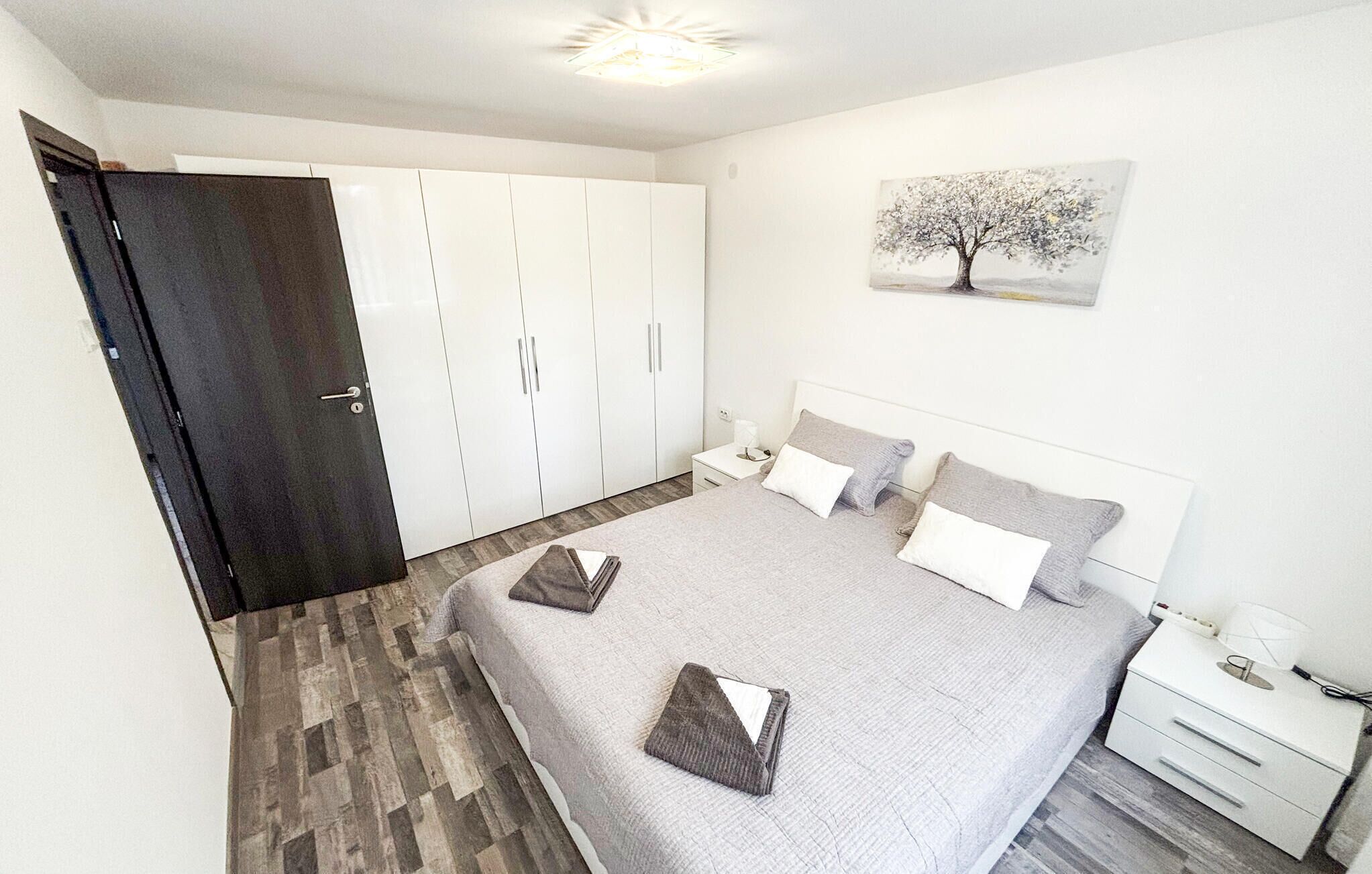 Un dormitorio con cama, mesitas de noche, un armario y un cuadro en la pared.