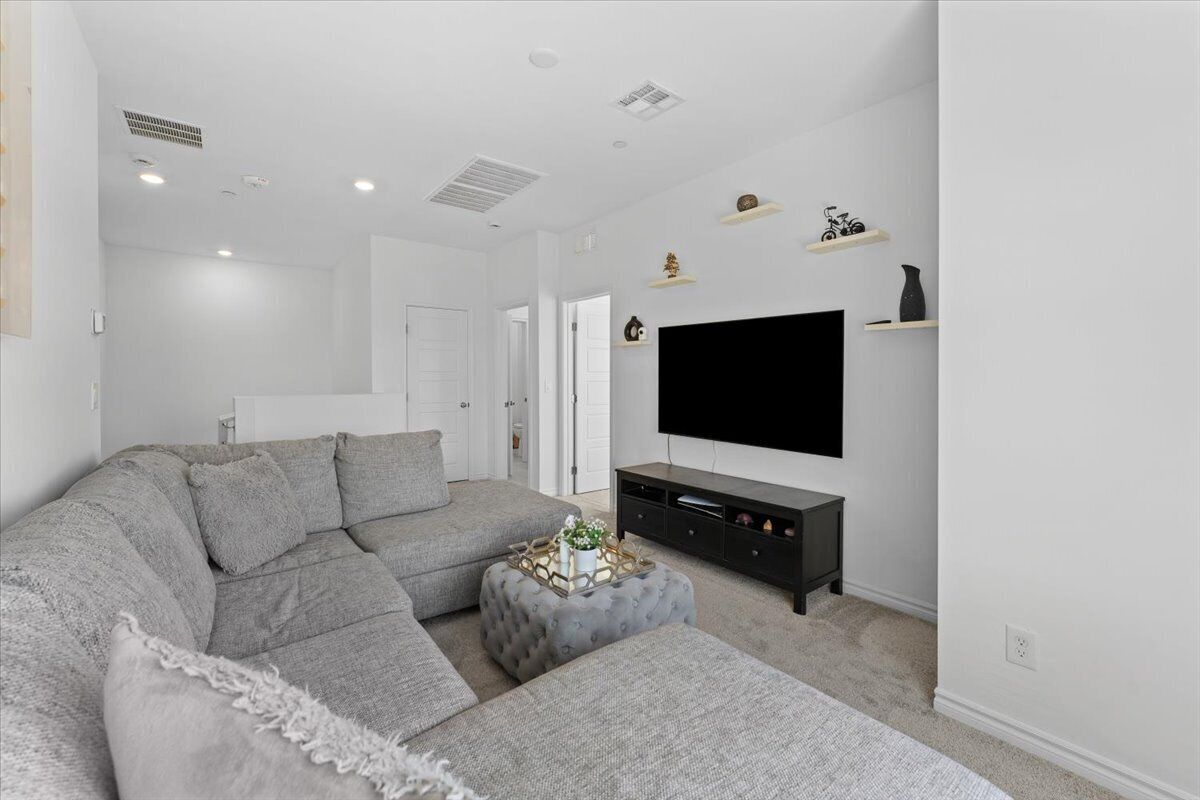 Una sala moderna con sofá seccional, reposapiés, televisor y decoración minimalista.