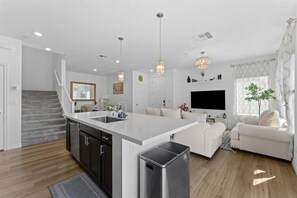 Eine moderne Küche mit einer zentralen Kochinsel, einem Essbereich mit einer Couch und einer Treppe, die zu einer oberen Ebene führt.