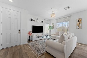 Ein Wohnzimmer mit Flachbildfernseher, einem weißen Sofa, einem Glastisch und einem dekorativen Teppich.