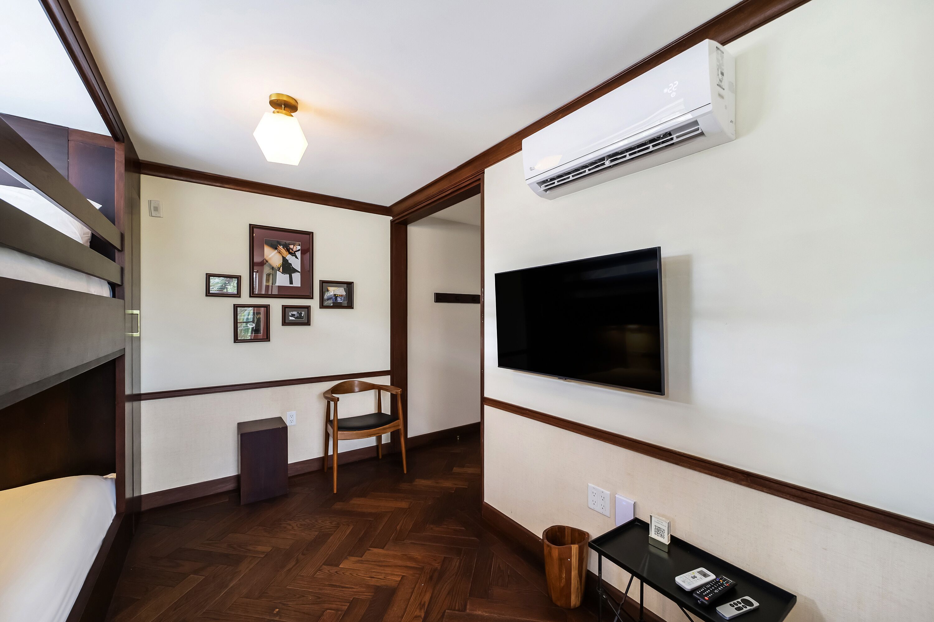Una habitació amb una llitera, televisió de pantalla plana, quadres al mur, una cadira de fusta, un safataixa i una taula petita amb un telèfon.