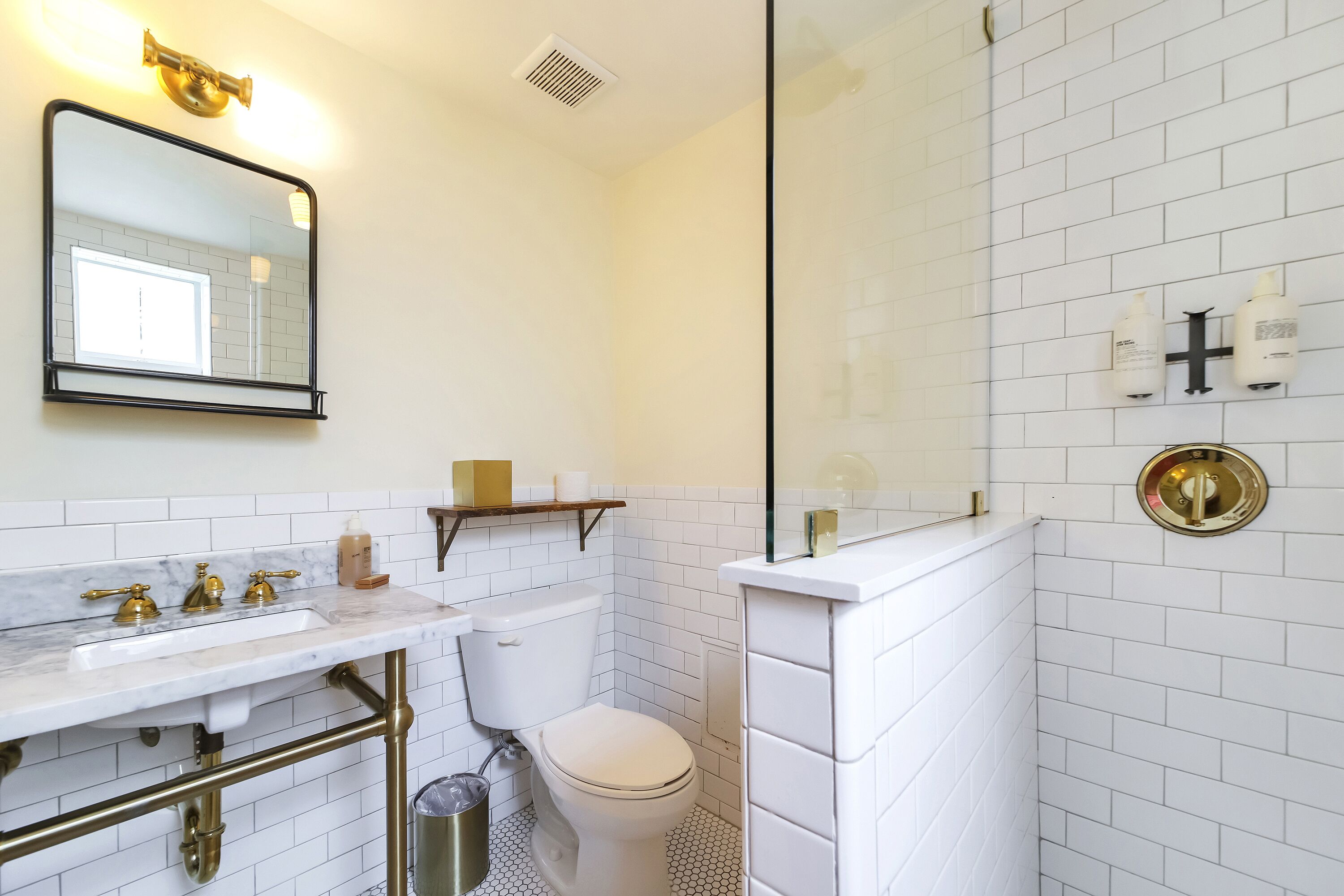 Une salle de bain avec une douche carrelée de carreaux blancs, un lavabo avec un robinet doré et des toilettes.